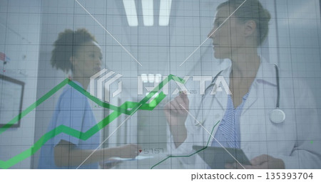 Doctor wearing white coat pointing at glass charts holding tablet in hospital corridor, copy space Doctor wearing white coat pointing at glass charts holding tablet in hospital corridor, copy space 135393704