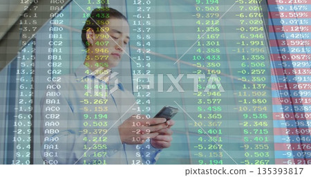 Examining floating market data, business professional holding smartphone in lobby with glass wall 135393817