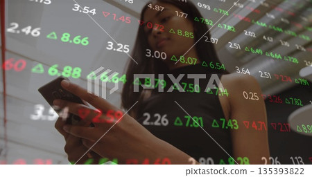 Businesswoman in sleeveless black top holding smartphone, reading stock figures on glass in office Businesswoman in sleeveless black top holding smartphone, reading stock figures on glass in office 135393822