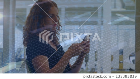 Woman holding smartphone, standing near wire mesh glass wall at lobby with benches and tables 135393839