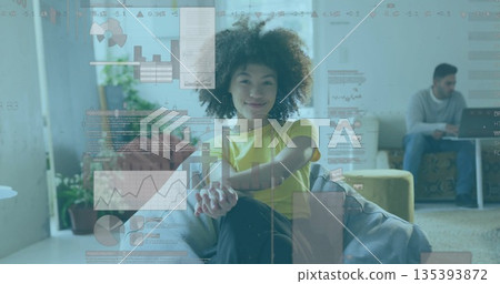 Sitting woman in yellow tee and jeans crossing legs in office lounge, with laptop, chart overlays 135393872