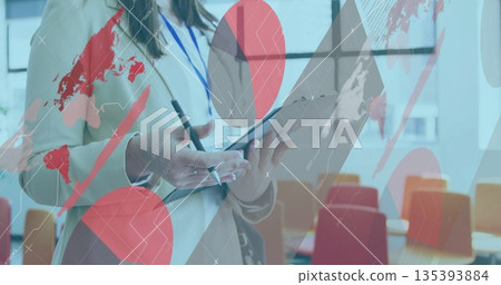 Holding tablet and stylus, woman wearing blazer and lanyard reviewing data overlays in boardroom 135393884