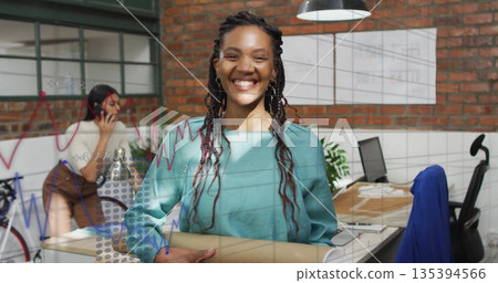 Smiling designer in teal blouse holding blueprint tube at loft office, with coworker talking phone Smiling designer in teal blouse holding blueprint tube at loft office, with coworker talking phone 135394566