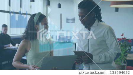 Collaborating woman in green top and man in white shirt using laptop and tablet in office 135394622