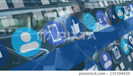 Leaning executives examining device screens near glass escalator railing, with floating icons 135394630