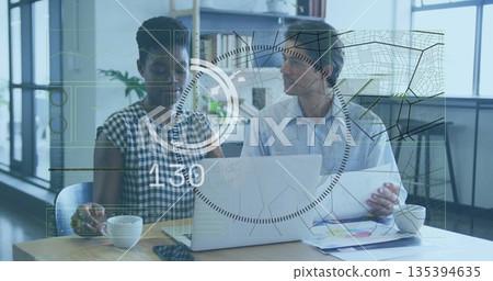 Two colleagues reviewing charts and checking smartphone at desk near windows, with circuit overlay Two colleagues reviewing charts and checking smartphone at desk near windows, with circuit overlay 135394635