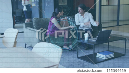 Discussing Indian woman and white man sitting on gray sofa at corporate lounge, with tablet laptop Discussing Indian woman and white man sitting on gray sofa at corporate lounge, with tablet laptop 135394639
