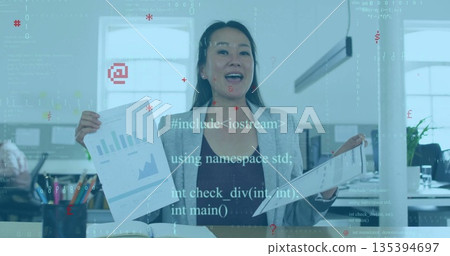 Presenting Korean woman wearing grey blazer displaying charts at office desk, with monitors Presenting Korean woman wearing grey blazer displaying charts at office desk, with monitors 135394697