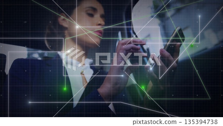 Holding smartphone with stylus pen, woman in dark blazer using digital network overlay in office Holding smartphone with stylus pen, woman in dark blazer using digital network overlay in office 135394738