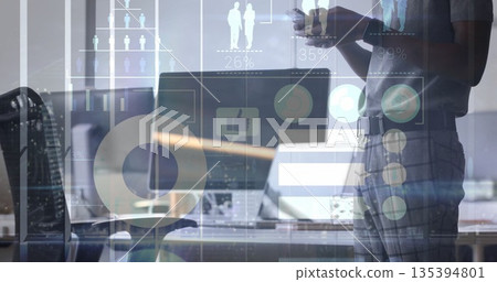 Holding smartphone worker standing beside desk in office with laptop-monitor and graphs, copy space Holding smartphone worker standing beside desk in office with laptop-monitor and graphs, copy space 135394801