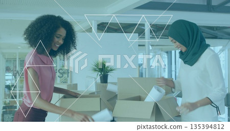 Unpacking coworkers in blouse, headscarf sorting cardboard boxes, plans at office with potted plant Unpacking coworkers in blouse, headscarf sorting cardboard boxes, plans at office with potted plant 135394812