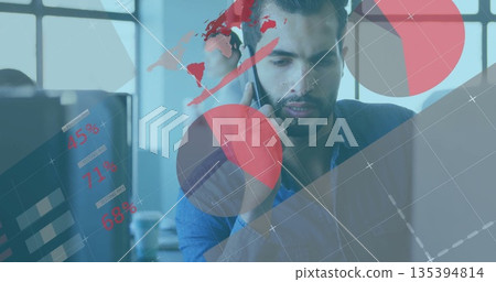 Speaking office worker holding smartphone and viewing laptop data in office, with digital charts 135394814