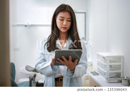 woman in white lab coat is looking at tablet woman in white lab coat is looking at tablet 135396043