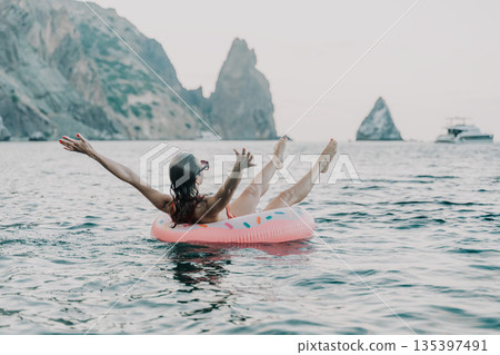 Woman, floating, sea. Relaxed woman enjoying summer vacation on an inflatable ring with mountains and copy space. Woman, floating, sea. Relaxed woman enjoying summer vacation on an inflatable ring with mountains and copy space. 135397491