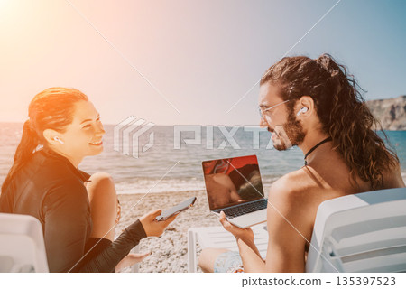 Beach Couple Laptop Sea - Young couple working on laptop and phone while relaxing on beach chairs. 135397523