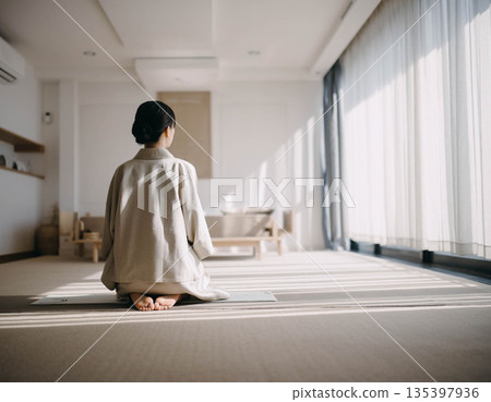 一位女士背對著鏡頭,坐在極簡主義的日式房間裡,自然光傾瀉而入。 一位女士背對著鏡頭,坐在極簡主義的日式房間裡,自然光傾瀉而入。 135397936