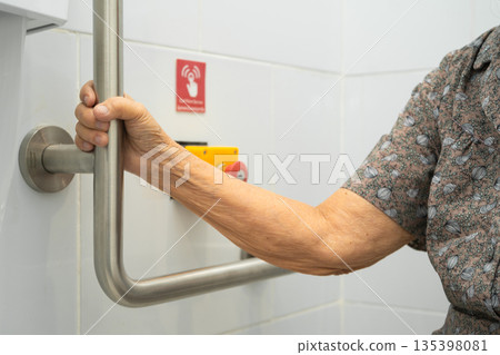 Asian elderly woman use toilet security support rail in bathroom. Asian elderly woman use toilet security support rail in bathroom. 135398081