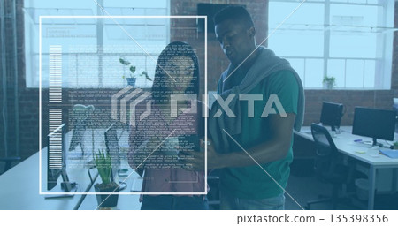 Collaborating software developers reviewing code and charts at open-plan office, with dual monitors 135398356