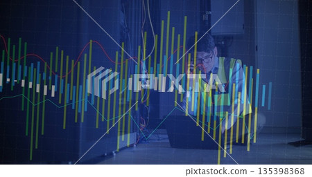 Crouching Korean engineer in safety vest checking laptop and phone in server room with rack, charts 135398368