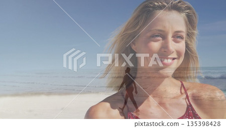 Smiling blonde woman wearing red sleeveless top posing by sandy beach, ocean waves and horizon 135398428