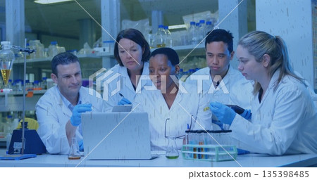Collaborating scientists analyzing data on laptop at research lab bench, with pipette and flasks 135398485