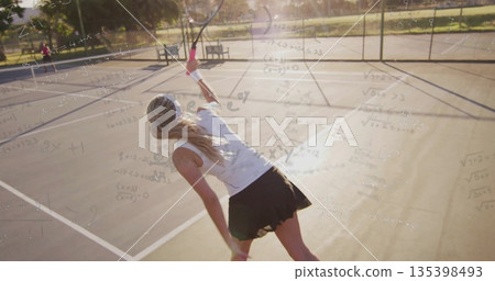 Serving tennis player wearing tennis skirt swinging racket on park court, with chain-link fence Serving tennis player wearing tennis skirt swinging racket on park court, with chain-link fence 135398493