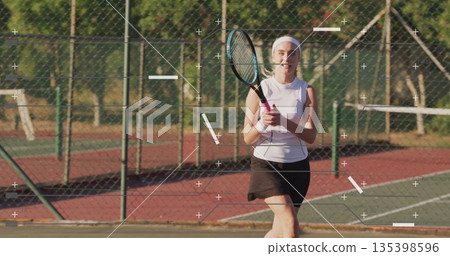 Preparing tennis player in white top gripping racket on painted park court, with chainlink fence 135398596