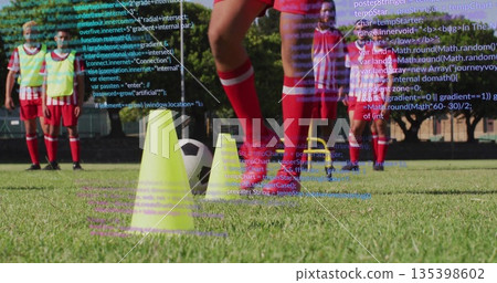 Red-jerseyed soccer player dribbling ball through cones, hurdles on grass field, with code overlay 135398602