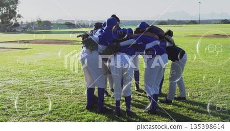Huddling baseball team wearing blue jerseys and gloves on sunlit field, with floating 6G icons Huddling baseball team wearing blue jerseys and gloves on sunlit field, with floating 6G icons 135398614
