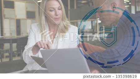 Gesturing colleagues in white and dark jackets viewing laptop in office lounge with overlay 135398619
