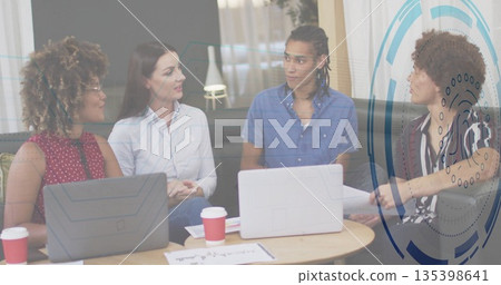 Collaborating colleagues around coffee table using laptops sipping coffee sorting papers in lounge 135398641