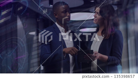 Collaborating professionals in suits analyzing data on tablet behind glass wall with digital charts Collaborating professionals in suits analyzing data on tablet behind glass wall with digital charts 135398657