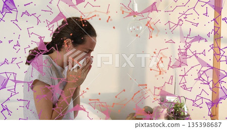 Sneezing adult woman blowing nose into tissue beside wooden table at home, geometric overlay Sneezing adult woman blowing nose into tissue beside wooden table at home, geometric overlay 135398687