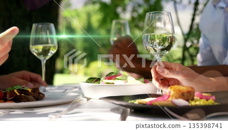 Trio holding wine glasses at white garden table with salads, grilled meat, corncake, pickles 135398741