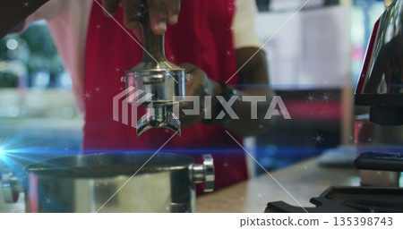 Red-apron barista tamping grounds behind cafe counter, with portafilter, knock box and tamper 135398743