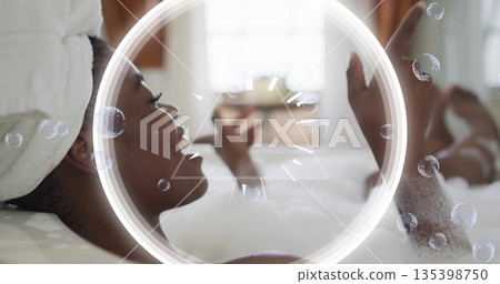 Relaxing woman raising arm in foamy bathtub by frosted window, with white towel turban, copy space Relaxing woman raising arm in foamy bathtub by frosted window, with white towel turban, copy space 135398750