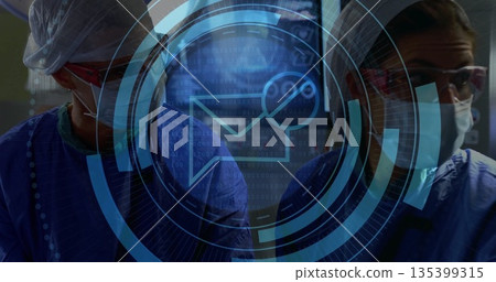 Standing female surgeons wearing masks, loupes and blue scrubs in operating room with HUD overlay 135399315