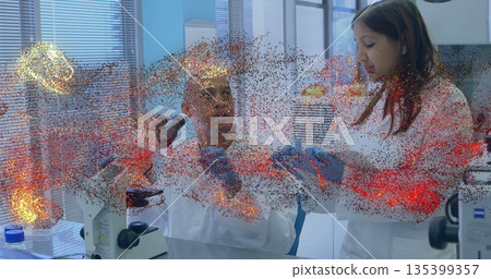 Examining woman scientist holding sample container while colleague studies with microscope in lab Examining woman scientist holding sample container while colleague studies with microscope in lab 135399357