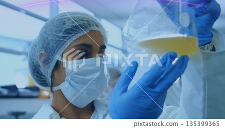 Inspecting lab technician wearing hairnet, mask, lab coat and gloves in lab, with Erlenmeyer flask 135399365