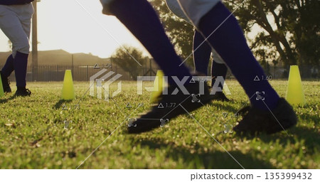 Running baseball player wearing white pants and cleats on grass field, with cones and data overlay 135399432