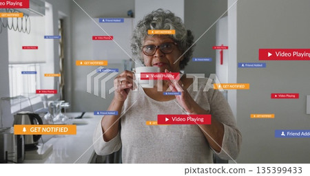 Woman wearing gray shirt tasting with spoon in kitchen, with floating colored notification banners 135399433
