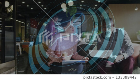 Coworkers discussing printed documents in office lounge, with coffee cup and workstation desks Coworkers discussing printed documents in office lounge, with coffee cup and workstation desks 135399442