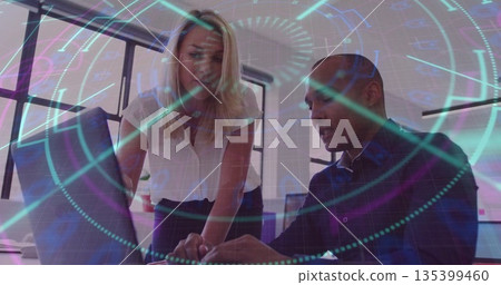 Collaborating mature business duo leaning over laptop in modern office, with holographic interface 135399460