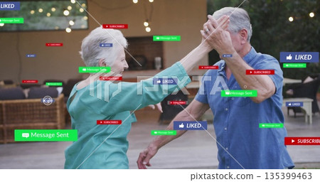 Dancing senior couple exchanging high-five on patio under string lights, with digital notifications Dancing senior couple exchanging high-five on patio under string lights, with digital notifications 135399463