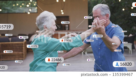 Dancing senior couple wearing turquoise blouse, blue shirt on patio, with floating social icons Dancing senior couple wearing turquoise blouse, blue shirt on patio, with floating social icons 135399467