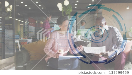 Reviewing documents, woman in sweater and man in shirt in office lounge with laptop, coffee cup 135399469