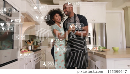 Dancing couple wearing aprons spinning at kitchen island, with chopping board and social icons Dancing couple wearing aprons spinning at kitchen island, with chopping board and social icons 135399647