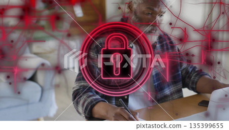 Typing man in plaid shirt working on laptop in living room workspace, with neon padlock overlay 135399655