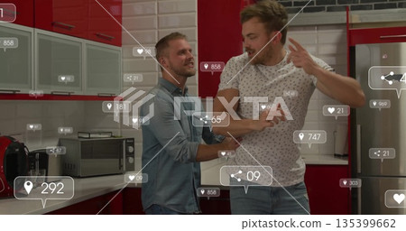 Interacting two men checking floating social media icons in kitchen with red cabinets and fridge 135399662