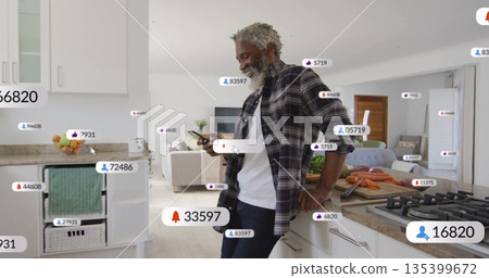 Plaid-shirted man leaning on modern kitchen island holding smartphone, with floating social metrics 135399672